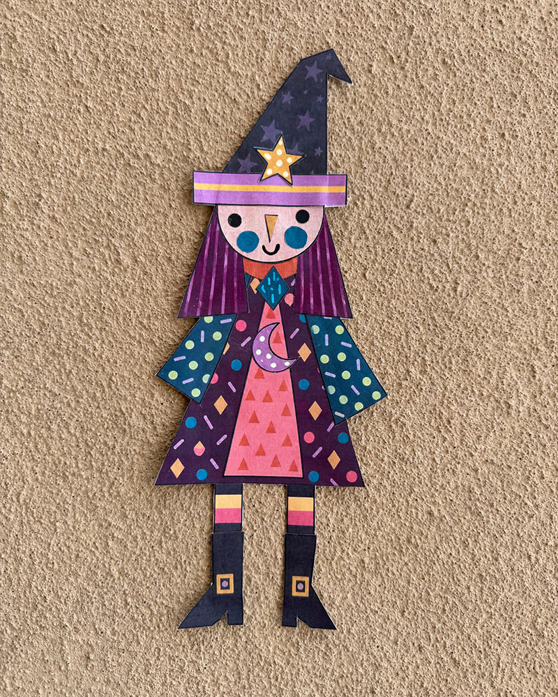 Handmade layered paper witch with colorful clothing, striped legs, and a star-covered hat